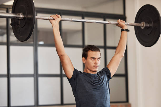 Focused man performing barbell overhead presses in a gym, an effective exercise for enhancing shoulder strength.