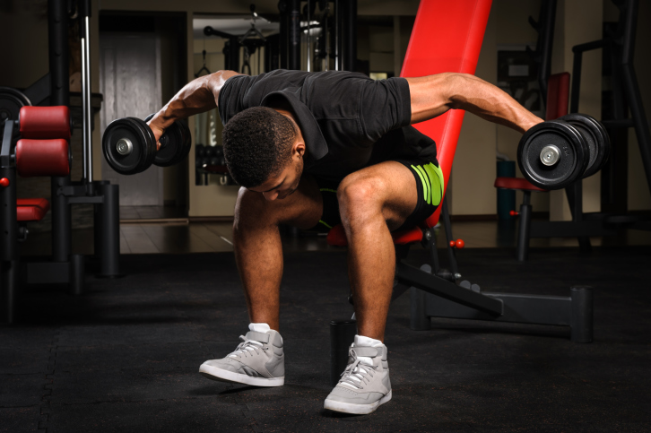 Individual performing bent-over reverse dumbbell flyes at the gym, targeting rear deltoids as part of a comprehensive shoulder workout.