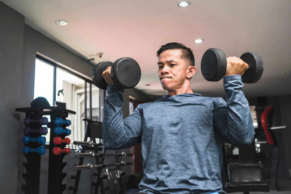 Man performing Arnold press with dumbbells at gym, an effective exercise for targeting multiple shoulder muscles, perfect for strengthening routines.