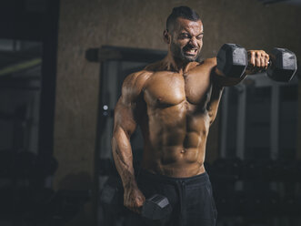 Man in gym performing dumbbell front raises to target the anterior deltoids.