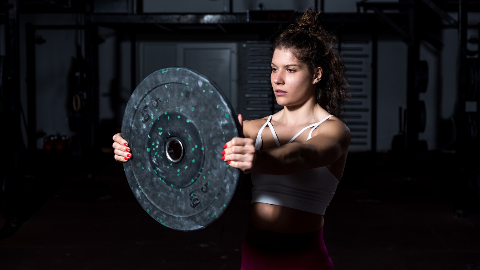 Female athlete performing a front plate raise in a gym, concentrating on her anterior deltoids for front shoulder strength.