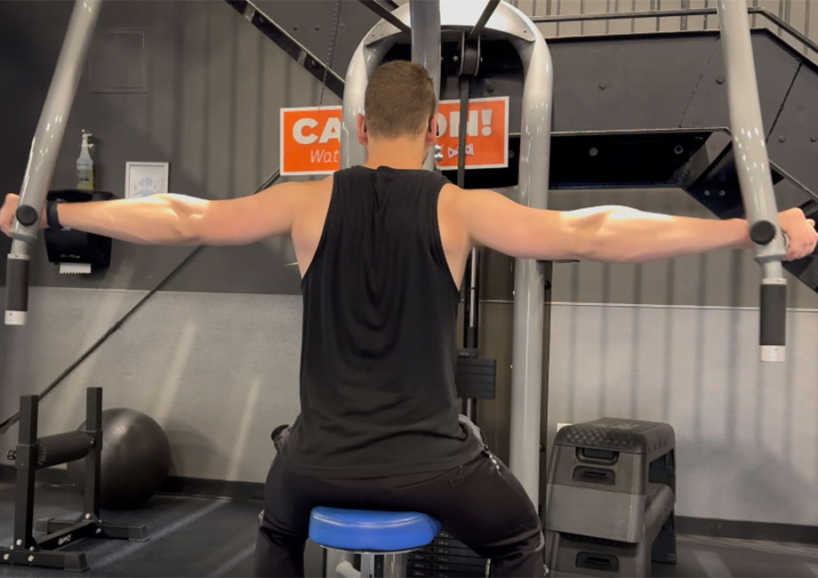 Man using reverse pec fly machine to work on rear deltoids, integral for balanced shoulder development in a top shoulder workout routine.