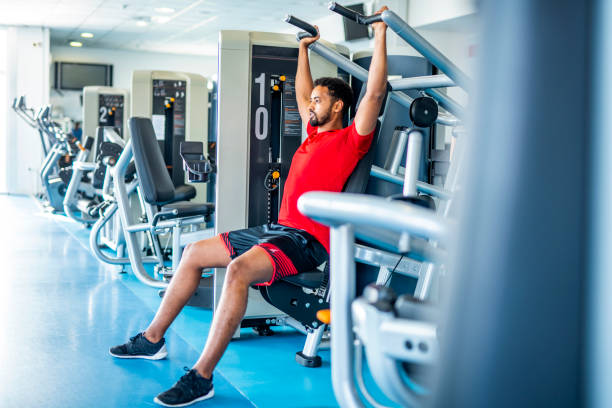 Man using a shoulder press machine at the gym, efficiently targeting the deltoid muscles for enhanced shoulder strength.