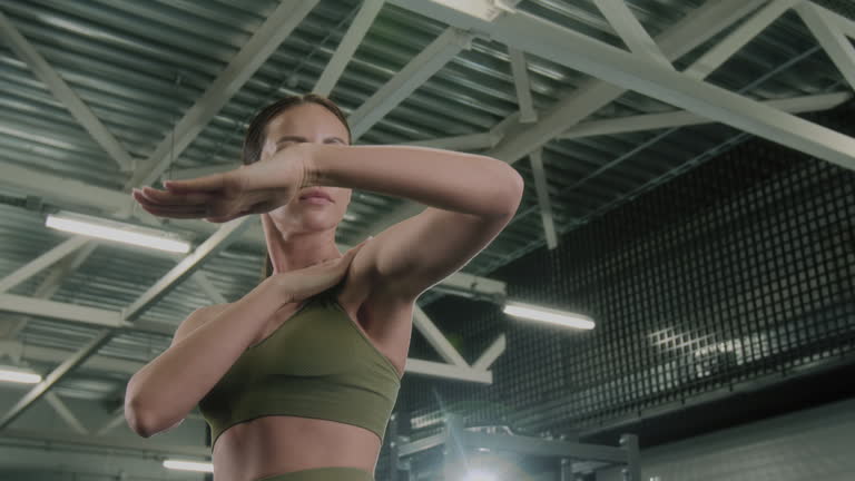 Fitness enthusiast performs a shoulder stretch in a gym setting, preparing her shoulders for a workout.