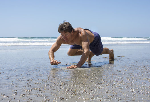 Man performing bear crawls on a sandy beach, demonstrating bodyweight shoulder exercises.