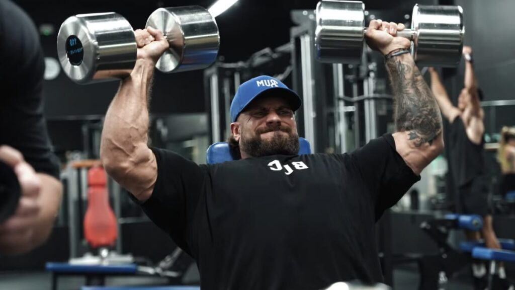 Chris Bumstead performing heavy dumbbell shoulder presses, a key exercise for building shoulder mass and strength.