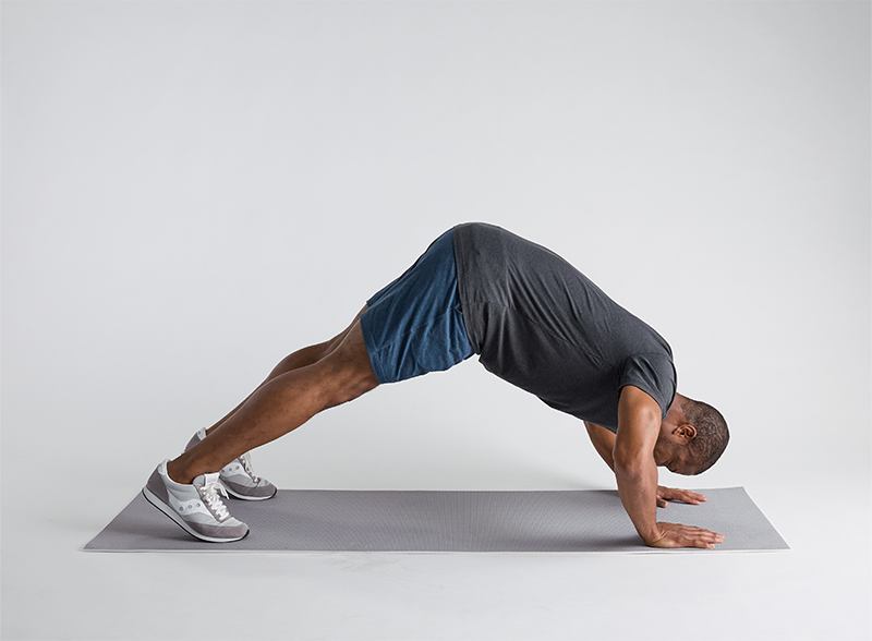 Man performing a pike pushup, a key bodyweight shoulder exercise, in a gym setting.