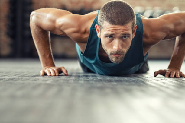 Man doing pushups on a gym floor, focusing on bodyweight shoulder exercises for strength.