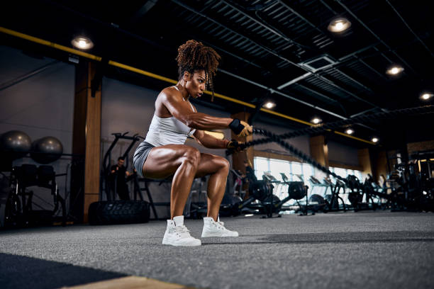 Motivated strong sporty lady performing the alternating waves exercise with battle ropes at the gym